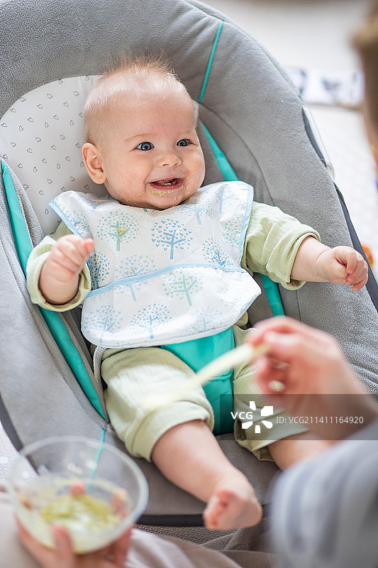 母亲用勺子喂坐在婴儿椅上的男婴图片素材