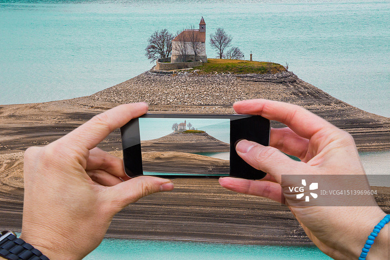男人用智能手机在法国湖边山顶拍摄教堂图片素材