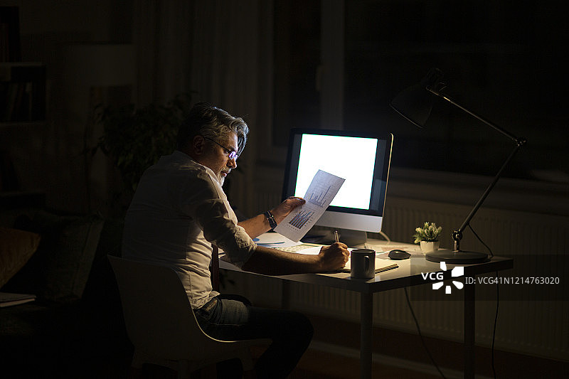 男子在深夜的家庭办公室写待办事项图片素材