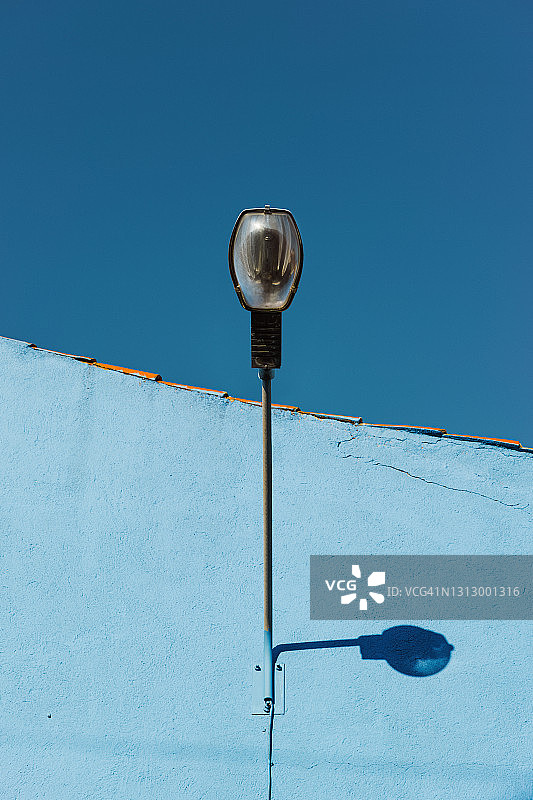 城市建筑的蓝色墙壁和蓝天下街灯的仰视视角图片素材