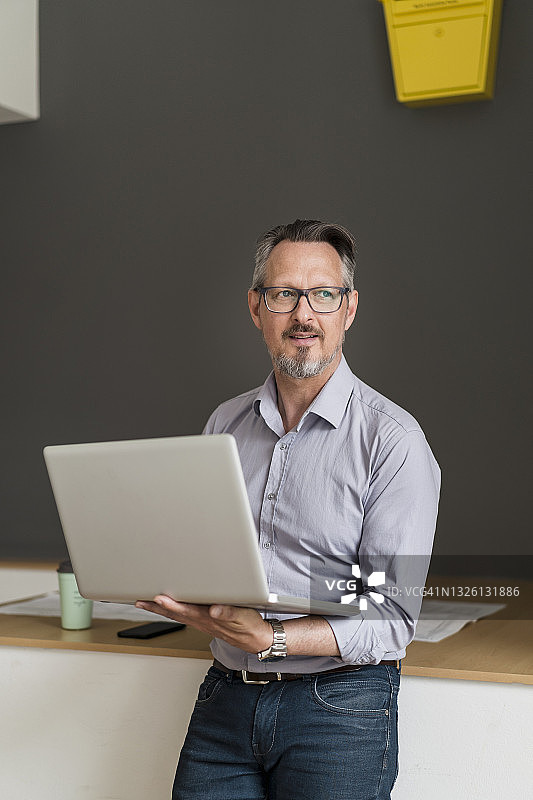 若有所思的商人拿着笔记本电脑望着办公室图片素材