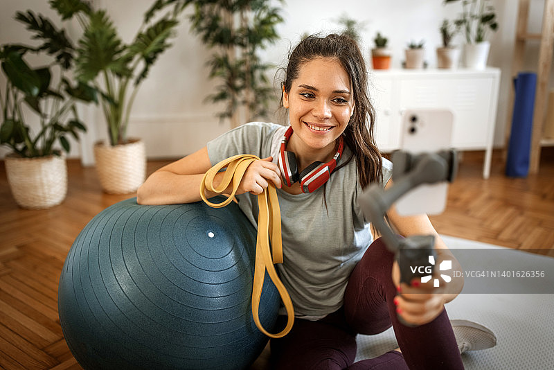 身穿运动服的活力女人坐在客厅地板上，用哑铃自拍图片素材