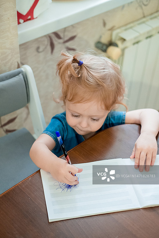 三岁女孩在厨房的桌旁学习写字图片素材