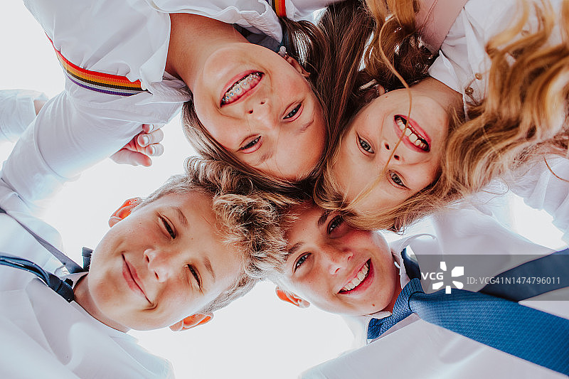 四个可爱的青少年孩子一起摆姿势微笑。从底部观看。图片素材