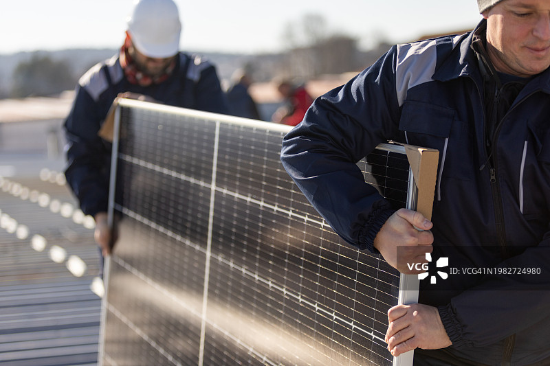 技师搬运光伏太阳能组件，同时在房屋屋顶上安装太阳能电池板系统图片素材