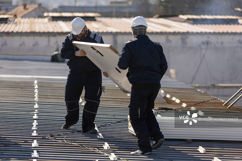 技师搬运光伏太阳能组件，同时在房屋屋顶上安装太阳能电池板系统图片素材