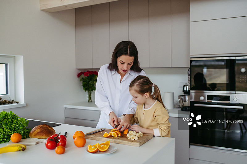 母亲在家和女儿一起做零食，烹饪。单亲妈妈和小朋友的周末活动。母亲节和母爱概念。图片素材