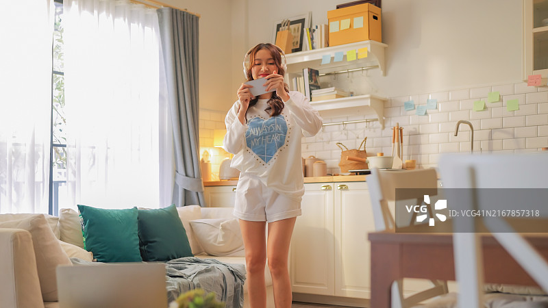 年轻的亚洲女性戴着耳机在家中兴奋地听音乐跳舞图片素材