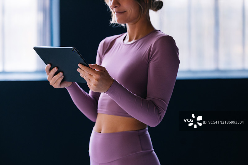 穿着运动服的女性在现代健身房中使用平板电脑图片素材