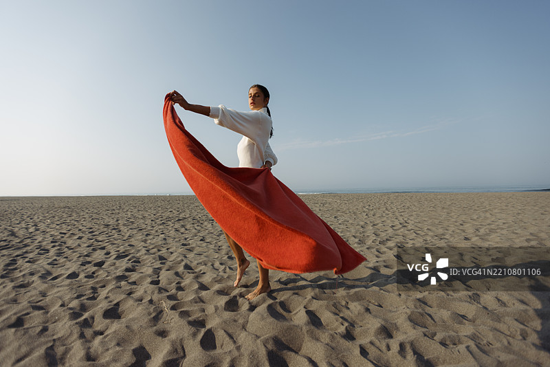 优雅的女人在沙滩上舞动着飘逸的布料图片素材