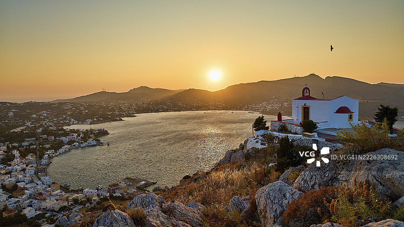 伊利亚斯教堂，浪漫的教堂场景坐落在山丘上，俯瞰日落时分的海湾，飞翔的鸟，阿尔金塔斯港，阿吉亚玛丽娜，莱罗斯，多德卡尼斯，希腊群岛，希腊图片素材