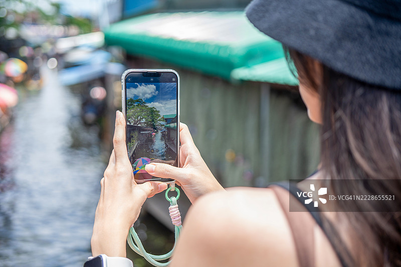 年轻女性游客在泰国的水上市场乘坐木船，品尝当地街头美食，享受东南亚之旅。图片素材