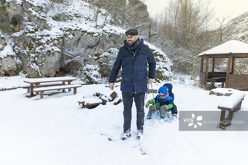 父亲在冬日户外拉着孩子们玩雪橇。图片素材
