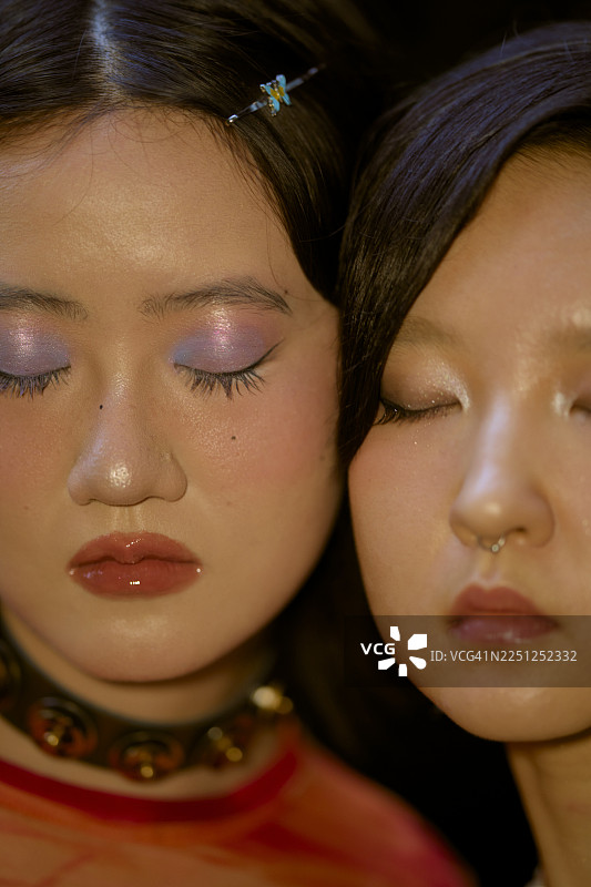 两位年轻女子闭着眼睛，化着色彩鲜艳的妆容，发型精致。中国上海。图片素材