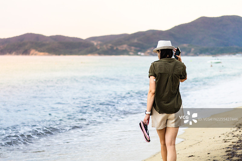 戴草帽的女子在海边。有了手臂上的持续葡萄糖监测仪、智能手表、手机和防水CGM保护套，糖尿病患者的旅行和生活都变得更轻松了。图片素材