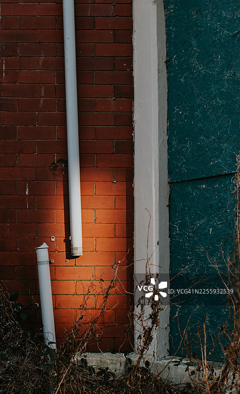 一处废弃的砖砌居民楼上，一根破损的白色塑料管道被低垂的阳光照亮图片素材